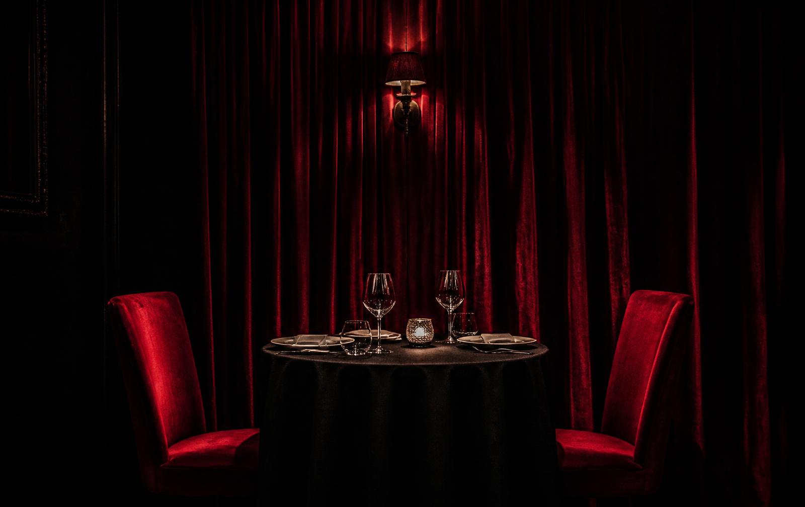 A candlelit table for two set against deep red velvet curtains